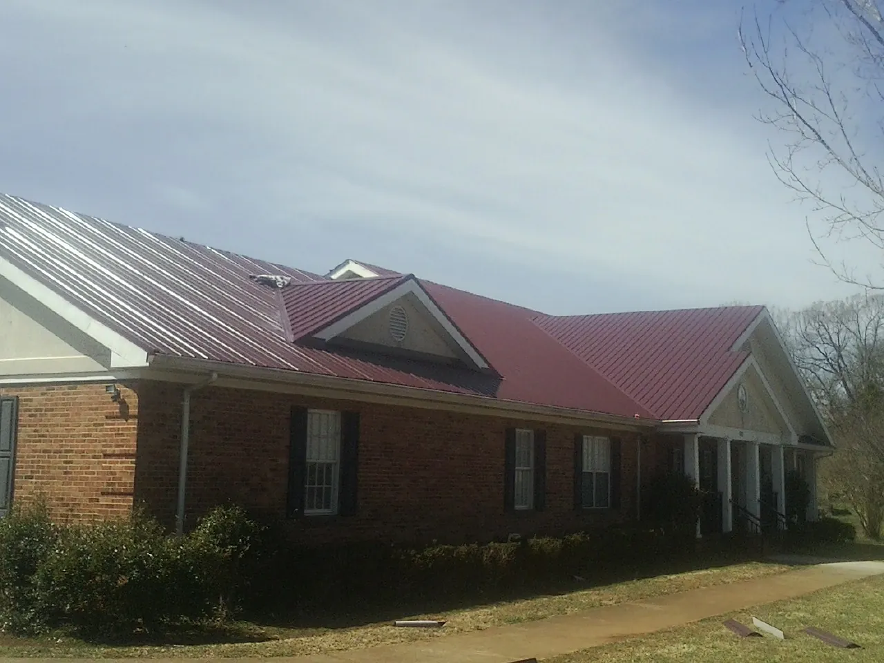 Red metal roof with gabled entries on a long brick building, from a Hail Damage Roof Repair job in Camp Dennison