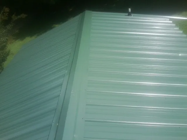New green metal panels meeting at the ridge of a roof — Flat Roof Repair work by our crew in Camp Dennison