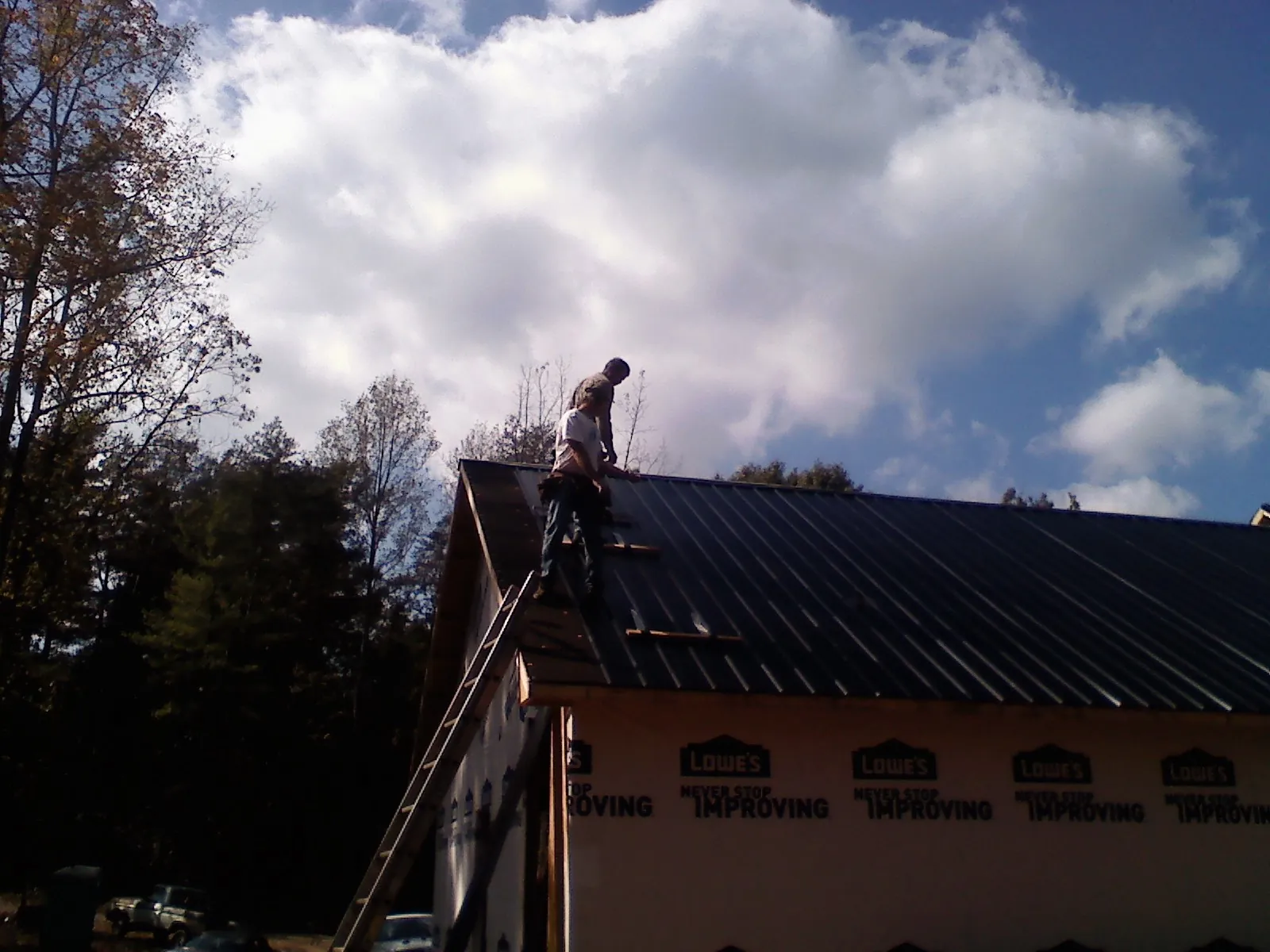 Roofer fastening dark metal panels high against a cloudy sky, from a Roof Inspection job in Camp Dennison