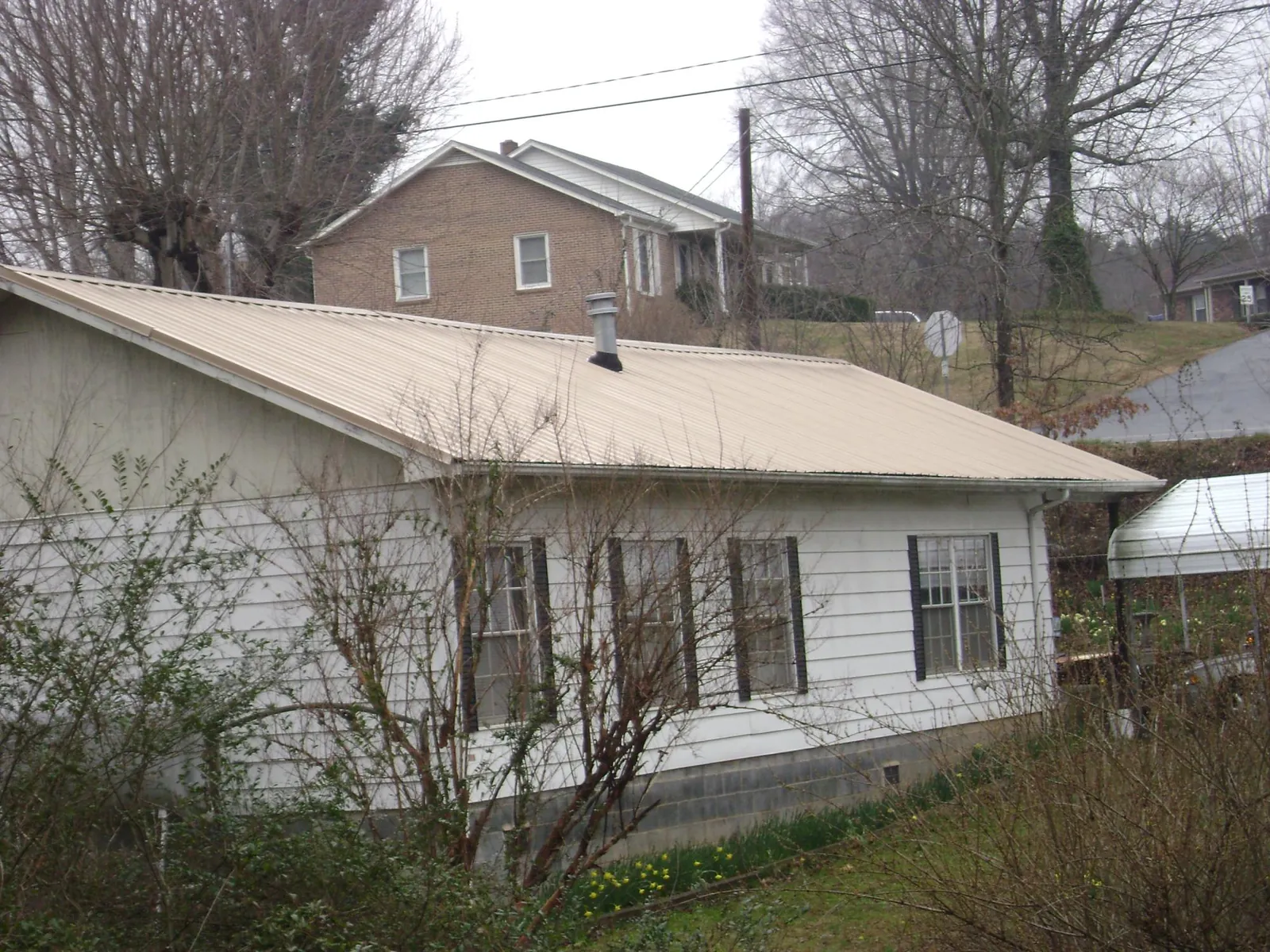 Tan metal roof on a white sided house set into a hillside — Commercial Roofing by Roofing Brothers in Camp Dennison